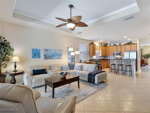 living room with light tile patterned flooring, a raised ceiling, visible vents, and crown molding