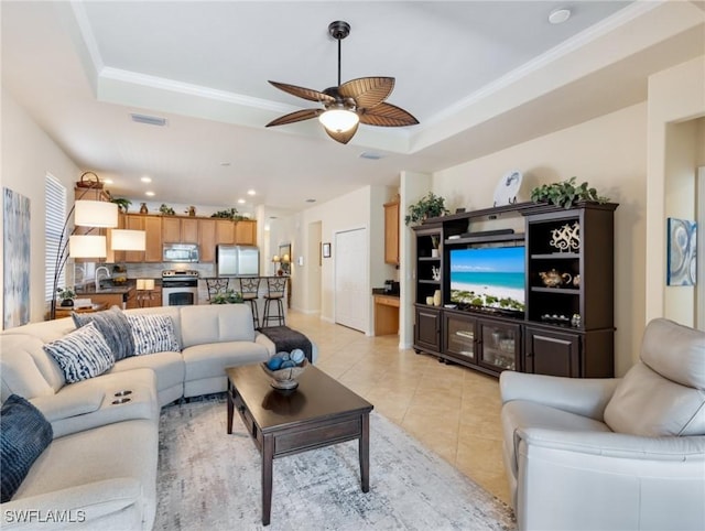 living area with ceiling fan, light tile patterned flooring, visible vents, ornamental molding, and a tray ceiling