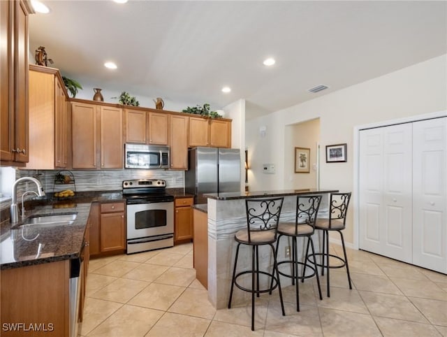 kitchen with a sink, stainless steel appliances, a kitchen bar, backsplash, and light tile patterned flooring