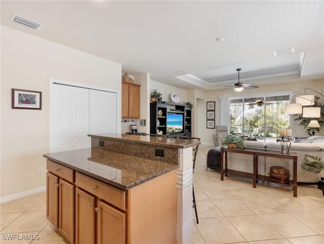 kitchen with a kitchen island, visible vents, open floor plan, a tray ceiling, and dark stone countertops