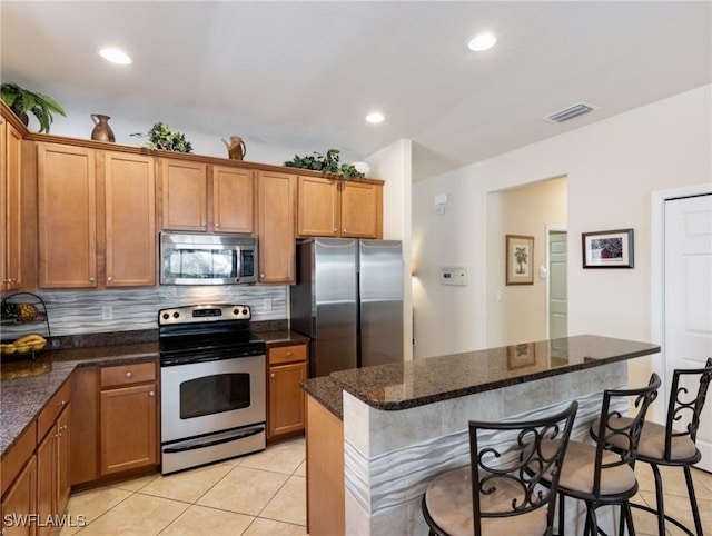 kitchen with a breakfast bar area, light tile patterned floors, stainless steel appliances, decorative backsplash, and brown cabinetry