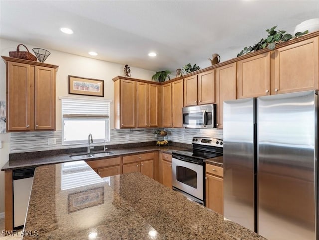 kitchen with decorative backsplash, appliances with stainless steel finishes, dark stone countertops, a sink, and recessed lighting