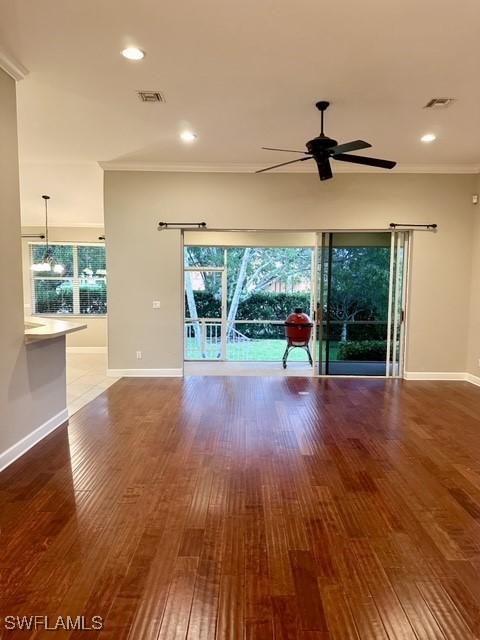 unfurnished living room with baseboards, visible vents, a ceiling fan, ornamental molding, and wood finished floors