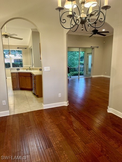 unfurnished dining area featuring light wood-type flooring, arched walkways, baseboards, and ceiling fan with notable chandelier