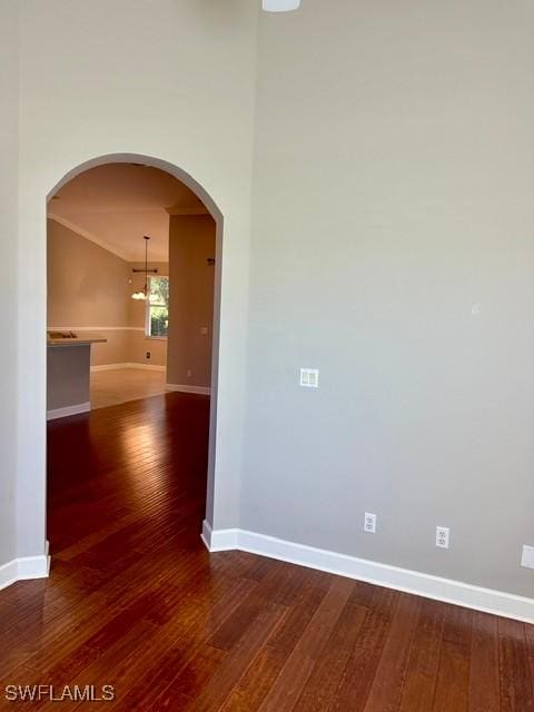 spare room featuring arched walkways, hardwood / wood-style flooring, and baseboards