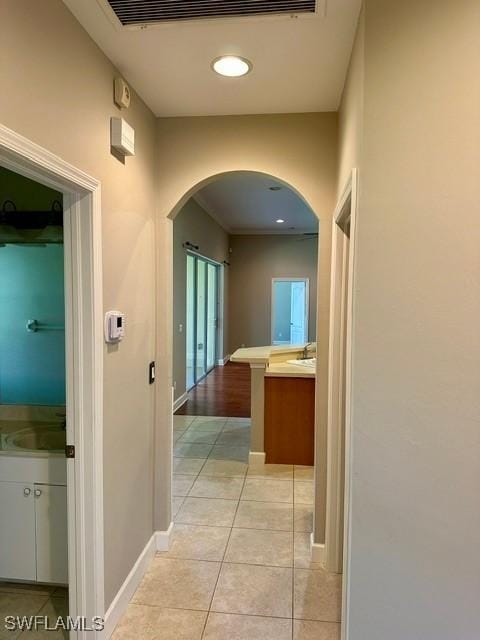 hallway featuring arched walkways, light tile patterned floors, and baseboards