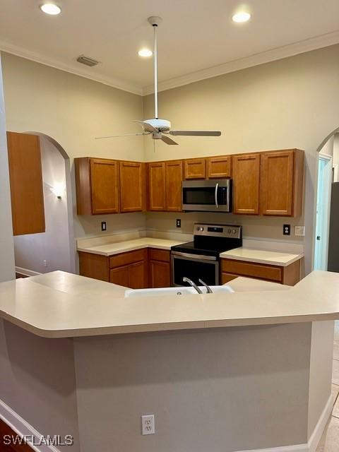 kitchen featuring arched walkways, light countertops, appliances with stainless steel finishes, and brown cabinetry