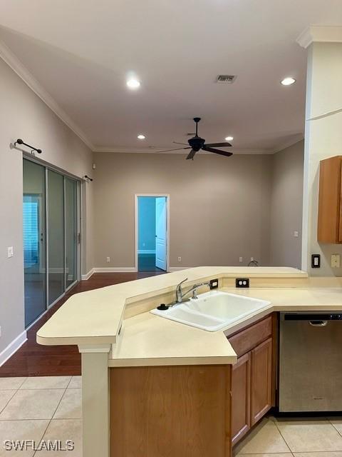 kitchen featuring light tile patterned floors, a sink, light countertops, dishwasher, and brown cabinetry