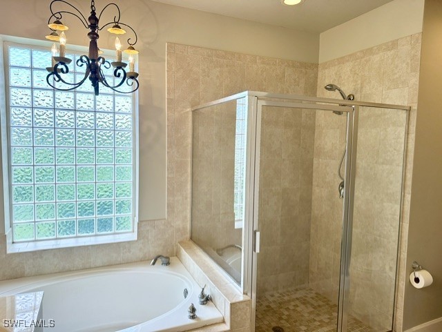 bathroom with a garden tub, a notable chandelier, and a shower stall