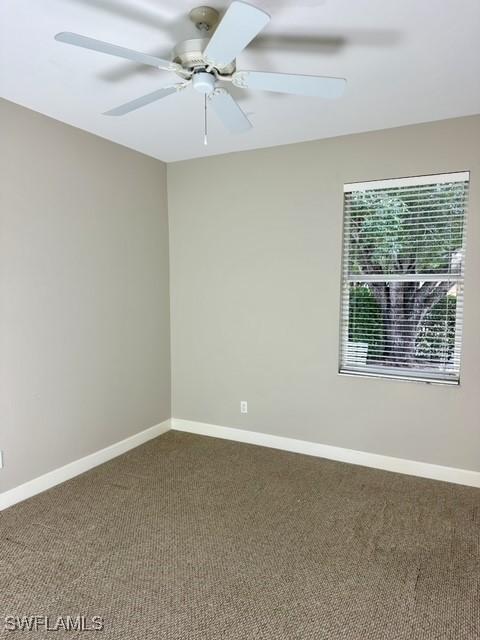 spare room with dark colored carpet, ceiling fan, and baseboards