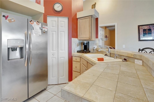 kitchen featuring tile counters, stainless steel refrigerator with ice dispenser, light brown cabinetry, and a sink