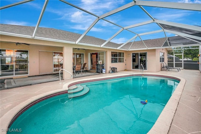 outdoor pool with glass enclosure, a patio, and a ceiling fan