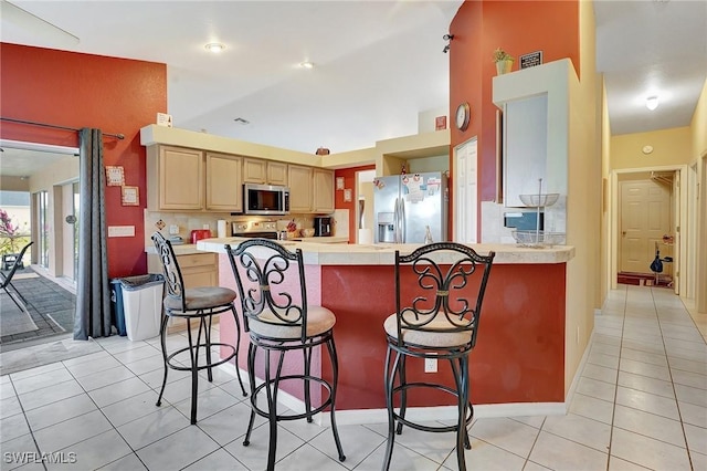 kitchen with light brown cabinetry, appliances with stainless steel finishes, a peninsula, light countertops, and light tile patterned floors