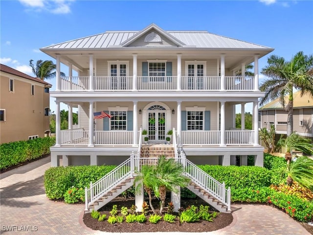 coastal home featuring decorative driveway, a porch, french doors, stairway, and metal roof