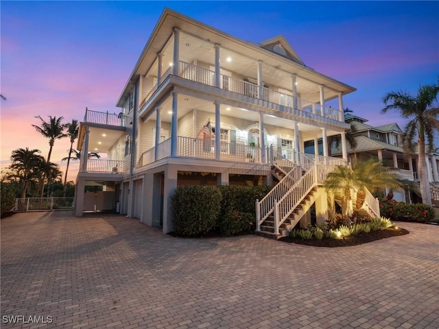 back of property at dusk with stairway, an attached garage, driveway, and a balcony