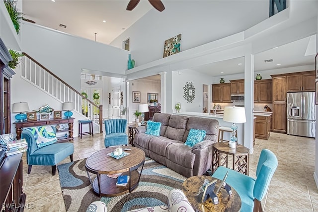 living area with light tile patterned floors, decorative columns, ceiling fan, stairs, and a towering ceiling