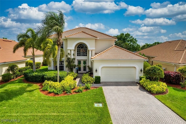 mediterranean / spanish-style home with a front lawn, decorative driveway, french doors, an attached garage, and a tiled roof