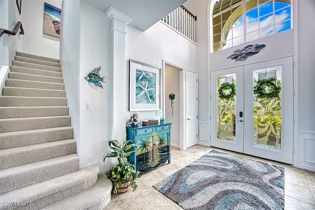 entryway featuring tile patterned flooring, stairs, french doors, a towering ceiling, and ornate columns