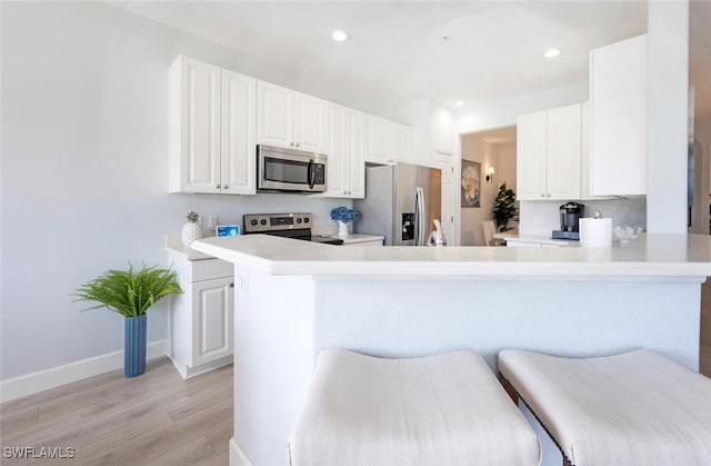 kitchen with a peninsula, white cabinetry, light countertops, appliances with stainless steel finishes, and light wood-type flooring