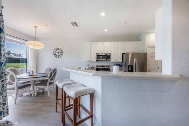 kitchen with pendant lighting, a breakfast bar area, stainless steel appliances, visible vents, and white cabinetry