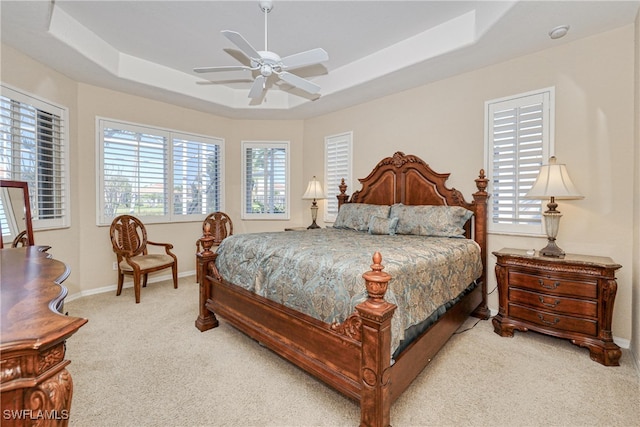 carpeted bedroom with baseboards, a raised ceiling, and a ceiling fan