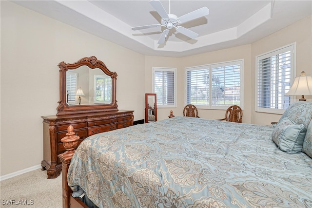 carpeted bedroom with a tray ceiling, multiple windows, baseboards, and ceiling fan