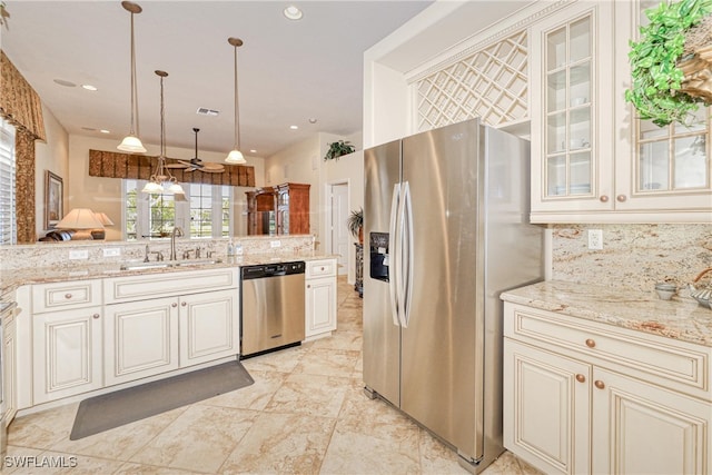 kitchen featuring cream cabinetry, a sink, tasteful backsplash, appliances with stainless steel finishes, and light stone countertops