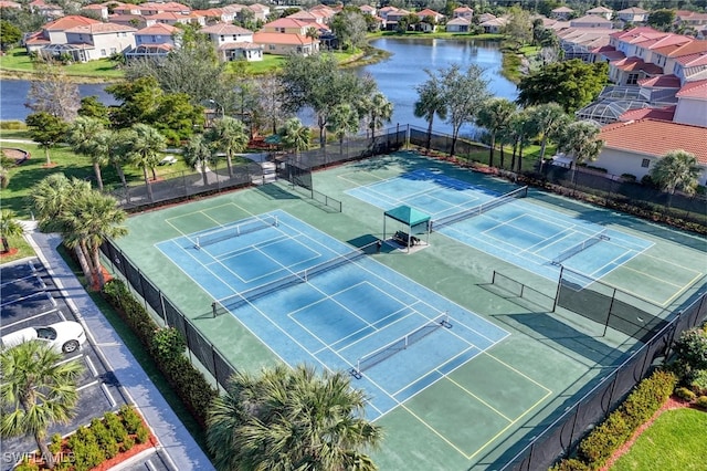 view of tennis court featuring a residential view, fence, and a water view