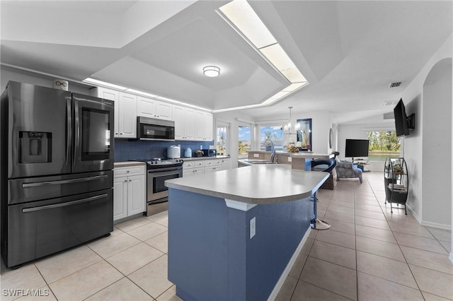 kitchen with stainless steel appliances, a raised ceiling, white cabinetry, and light tile patterned floors