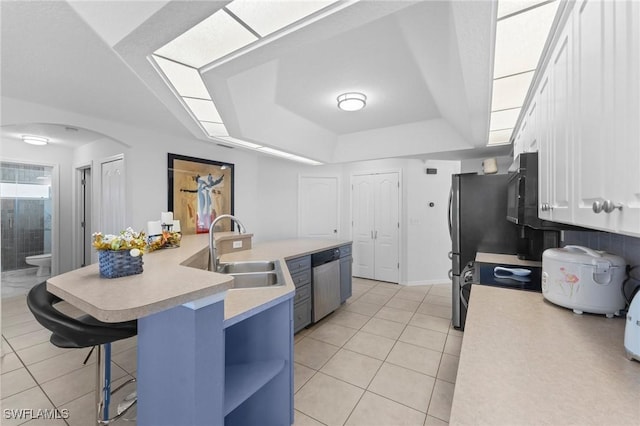 kitchen with a tray ceiling, stainless steel appliances, light countertops, a sink, and light tile patterned flooring