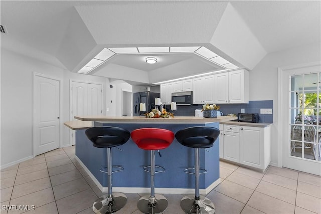 kitchen featuring white cabinets, light tile patterned floors, a breakfast bar, and black fridge