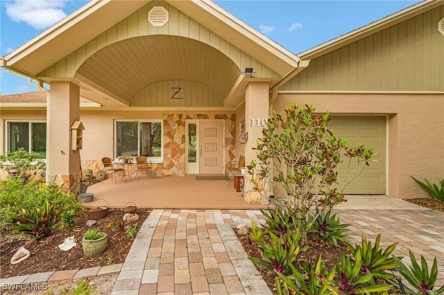 property entrance with covered porch, stucco siding, and an attached garage