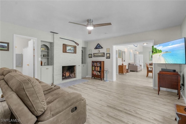 living room featuring light wood-style flooring, built in features, baseboards, a brick fireplace, and ceiling fan