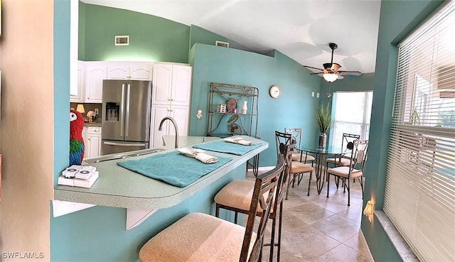 kitchen featuring stainless steel fridge with ice dispenser, visible vents, white cabinetry, vaulted ceiling, and a kitchen breakfast bar