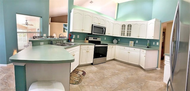 kitchen featuring a peninsula, a sink, white cabinetry, appliances with stainless steel finishes, and glass insert cabinets