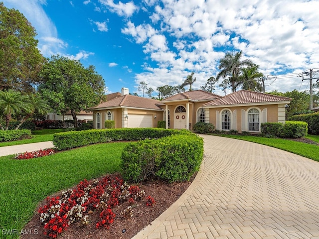 mediterranean / spanish-style house featuring a tiled roof, a front yard, decorative driveway, and stucco siding