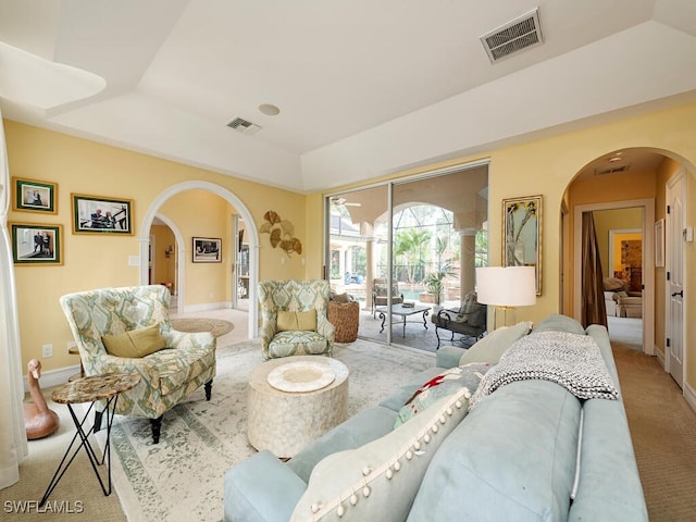 living room with carpet floors, arched walkways, visible vents, and a tray ceiling