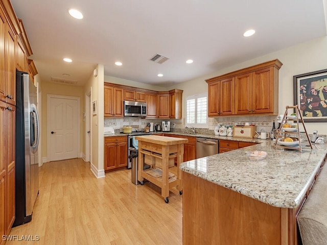 kitchen with visible vents, appliances with stainless steel finishes, brown cabinetry, light wood-style floors, and a peninsula