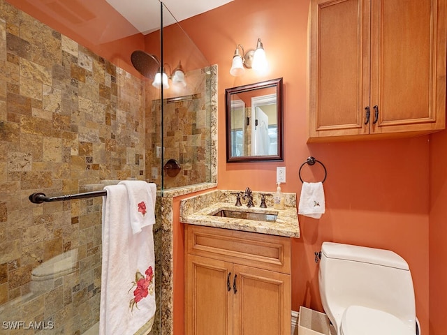 bathroom with toilet, tiled shower, and vanity