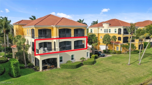 back of property with a tile roof, a yard, a balcony, and stucco siding