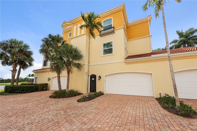 view of front of house with decorative driveway, a tile roof, a balcony, and stucco siding