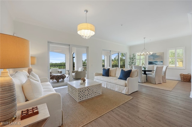 living room featuring a wealth of natural light, ornamental molding, a notable chandelier, and wood finished floors