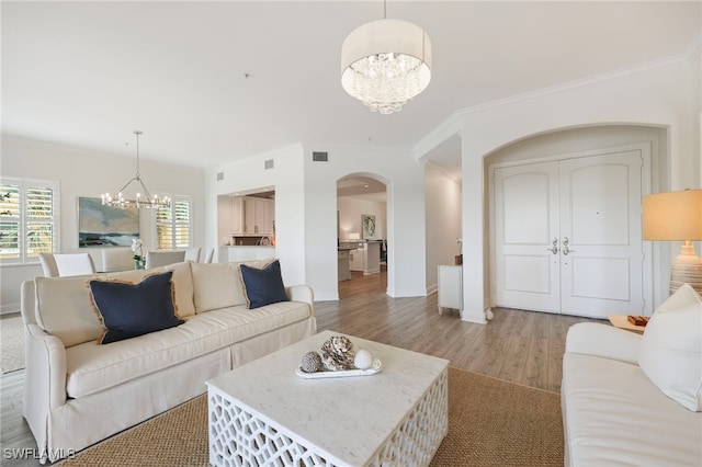 living area with arched walkways, crown molding, visible vents, an inviting chandelier, and light wood-type flooring