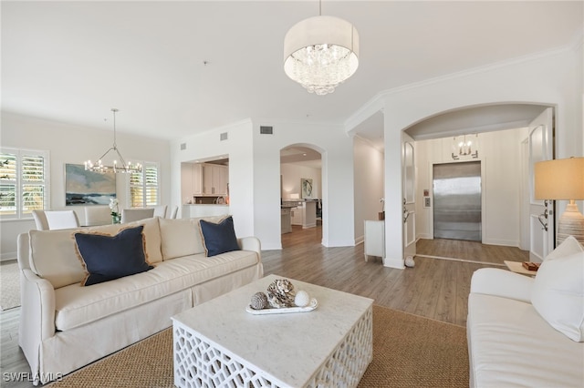 living room with arched walkways, visible vents, light wood-style flooring, ornamental molding, and a chandelier