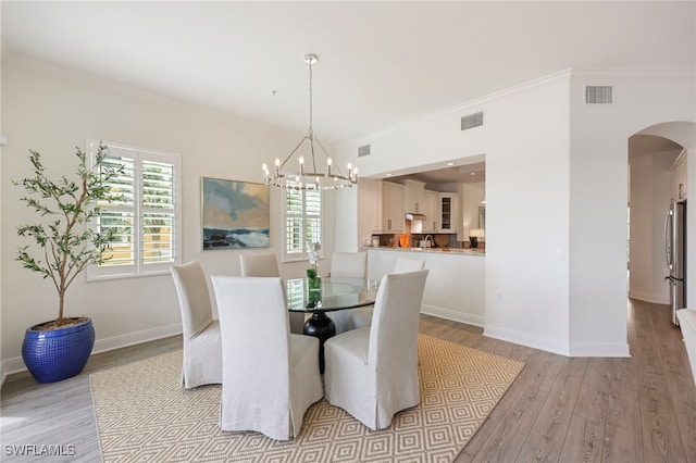 dining area featuring light wood-style floors, visible vents, arched walkways, and crown molding