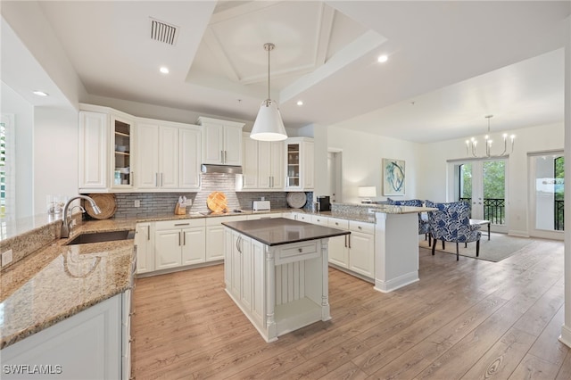 kitchen featuring light wood-style flooring, under cabinet range hood, a peninsula, a sink, and visible vents