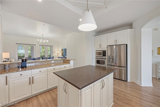 kitchen with hanging light fixtures, appliances with stainless steel finishes, white cabinets, dark stone countertops, and light wood-type flooring