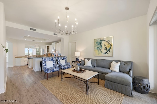 living room with light wood-style floors, visible vents, a chandelier, and a raised ceiling