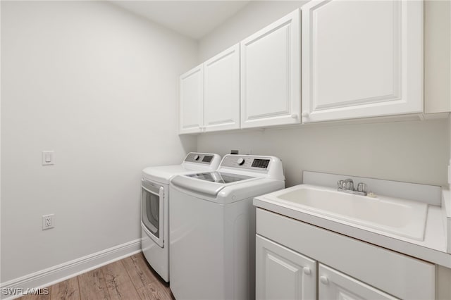 laundry room with washing machine and dryer, light wood-style flooring, a sink, baseboards, and cabinet space