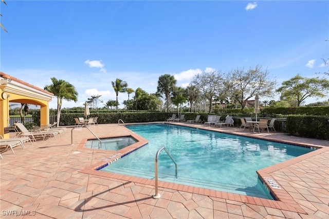 community pool with a patio area, fence, and a hot tub